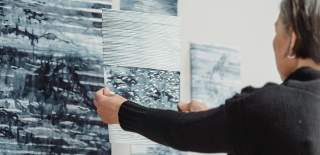 A woman hangs grey portraits on a gallery wall in preparation for an exhibit
