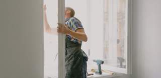 A man restores a window with a drill on the window sill