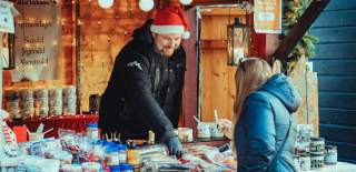 Mann som selger diverse delikatesser fra bod under julemarkedet i Sarpsborg. Foto.