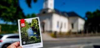 En hånd holder i en brosjyre for Borgleden foran en kirke