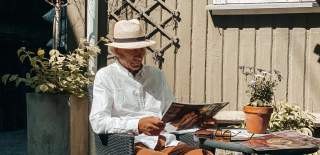 Mann med hatt som sitter og leser avisen på et kafébord i Sarpsborg. Foto.