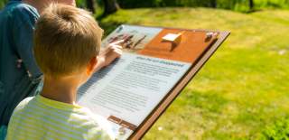 To gutter studerer plakater ved kulturminner - her gravhaug