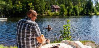En mann som sitter på piknikpledd mens damen bader i bakgrunn