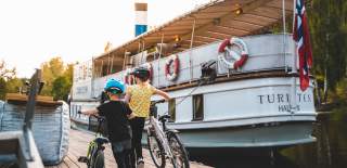 To barn som triller sykkelen ved siden av båten Turisten