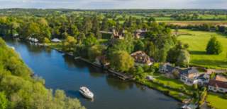 a boat cruising along the river thames surrounded by countryside.