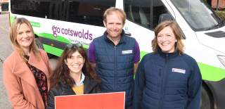 Four people smiling at the camera in front of a Go Cotswolds minibus holding up a red placard reading English Tourism Week