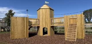 A wooden outdoor castle themed climbing frame