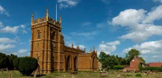 A picture of a church in field beneath a cloudy blue sky