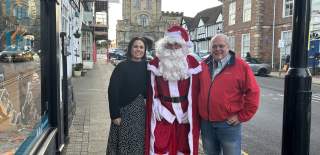 A photo of two people standing on Smith Street in Warwick with Santa Claus standing between them. All threee are smiling at the camera.