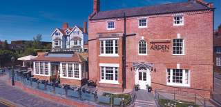 A frontal view of a red brick hotel with a front terrace beneath a clear blue sky
