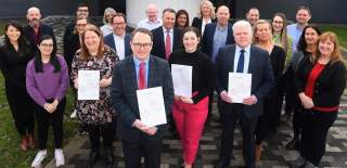 A group of people in business dress smiling at the camera whilst holding certificates