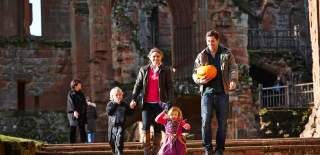 A family walking down stone steps at an outdoor castle. Children are in Halloween costume and the man is carrying a pumpkin
