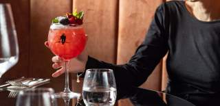 Close up of someone holding a red colour cocktail in a round glass with stem