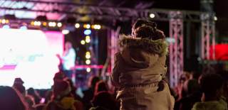 Girl sitting on man's shoulders to see guitarist on stage at Countdown to Christmas event