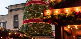 Christmas Market chalet lit up in daytime with Christmas tree in the background