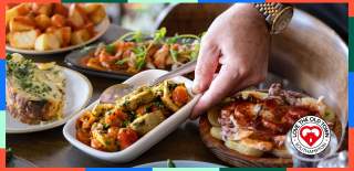 Man placing down dish of roasted vegetables among other Spanish, Mediterranean dishes at La Regata
