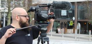 A person stood behind a camera filming in Guildhall Square