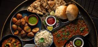 Mixture of vegetarian Indian dishes on large round serving plate including naan bread, lentil curries and chutneys