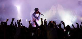 Person singing on a foggy stage with a crowd in front of them and hands in the air