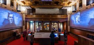 Inside the Titanic Exhibition at Seacity museum with people looking at information boards and screens on either side of the room