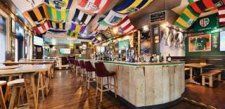 Inside of Shenanigans Irish bar with high tables and flags on the ceiling.