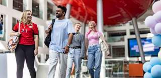 Four students walking inside The Spark building at Solent University smiling and talking. There is a red ppod-styleroom in the background