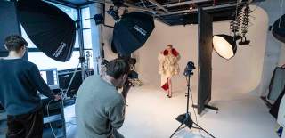 A photoshoot with a fashion model posing in front of cameras and lights with a white background