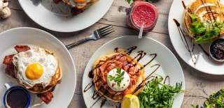 Spread of fluffy pancakes topped with breakfast toppings such as eggs and bacon, with a berry smoothie on the side