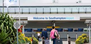 Two people with suitcases walking across the road into Southampton Airport