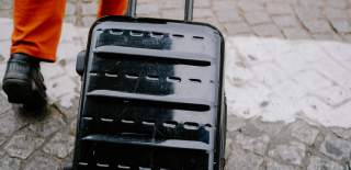Close up of a black suitcase and someones feet pulling it along
