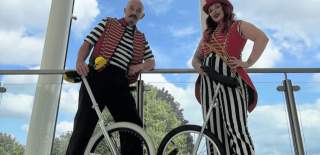 Two people dressed in traditional circus clothes stood holding unicycles.