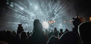 A crowd stands in silhouette in front of a light projection coming forwards