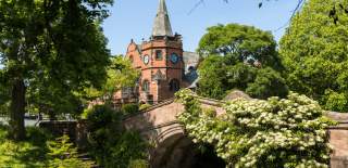 A red brick church and bridge surrounded by large, green trees