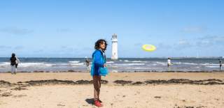 A child plays frisbee on a sunny beach with a lighthouse in the distance
