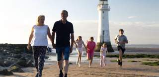 A family walk along the beach with New Brighton Lighthouse in the background