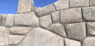A wall made from mismatched, grey cement blocks against a blue sky