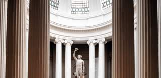 A white sculpture of a naked man inside a Grecian, domed building