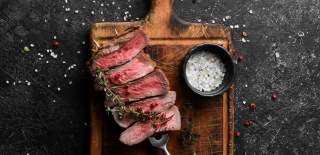 A  rare steak on a skewer in a wooden chopping board with rock salt next to it