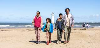 A family walk along New Brighton beach with New Brighton Lighthouse in the background.