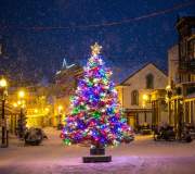 A Christmas tree with multicolored lights sparkles in the middle of Mackinac Island’s snowy Main Street on a winter night