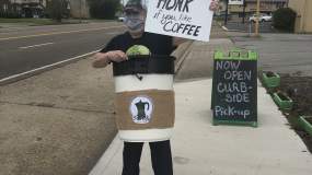 A man dressed as a Perk City Coffee drink advertises their curbside pickup option for patrons.