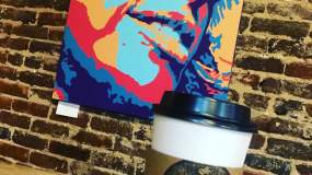 A brightly-colored painting decorates the wall behind a fresh cup from Awaken Coffee.