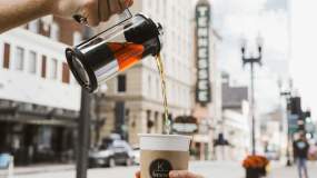 Fresh tea from K. Brew is poured into a cup held by an outstretched hand.