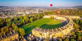 An aerial view of the Royal Crescent in Bath near Bristol, with hot air balloons launching from the green