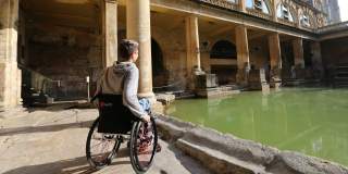 A man in a wheelchair looking at the Great Bath at The Roman Baths