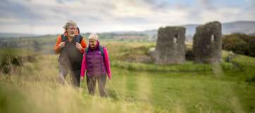 A couple enjoying a walk around the site of Harry Avery's castle with ruins in the background