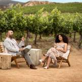 Man and woman sitting in chairs with rolling vineyards behind them, relaxing with eyes closed.