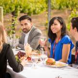 A group of friends enjoys a meal at a vineyard, outdoors