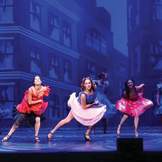 Three female dancers in colorful costumes dance on a stage