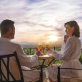 A couple sits overlooking a valley in Temecula, toasting with glasses of sparkling wine